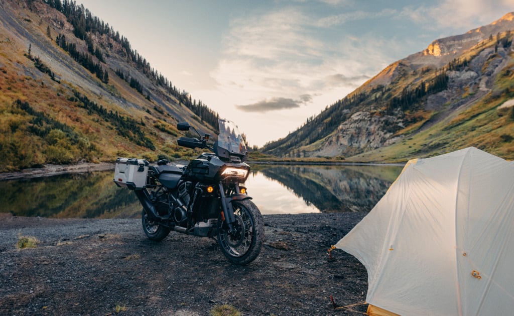 2024 Pan America out in the wilderness with mountains and a tent set up besides it.
