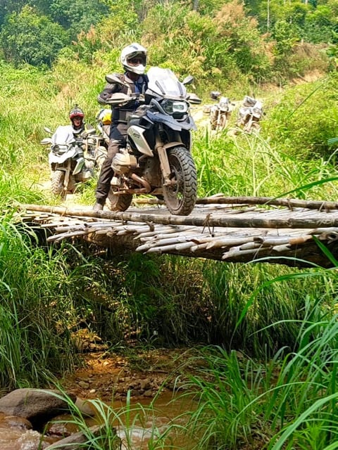 Customer of RIDE Adventures crossing a bamboo bridge in Thailand on his motorcycle.