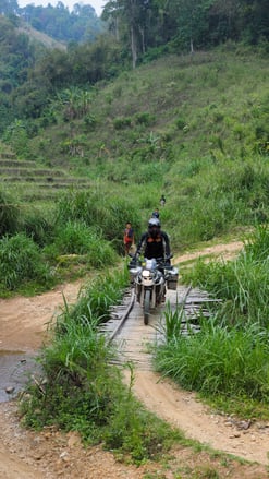 ADV Motorcycle riding across a bamboo bridge in Thailand in the jungle