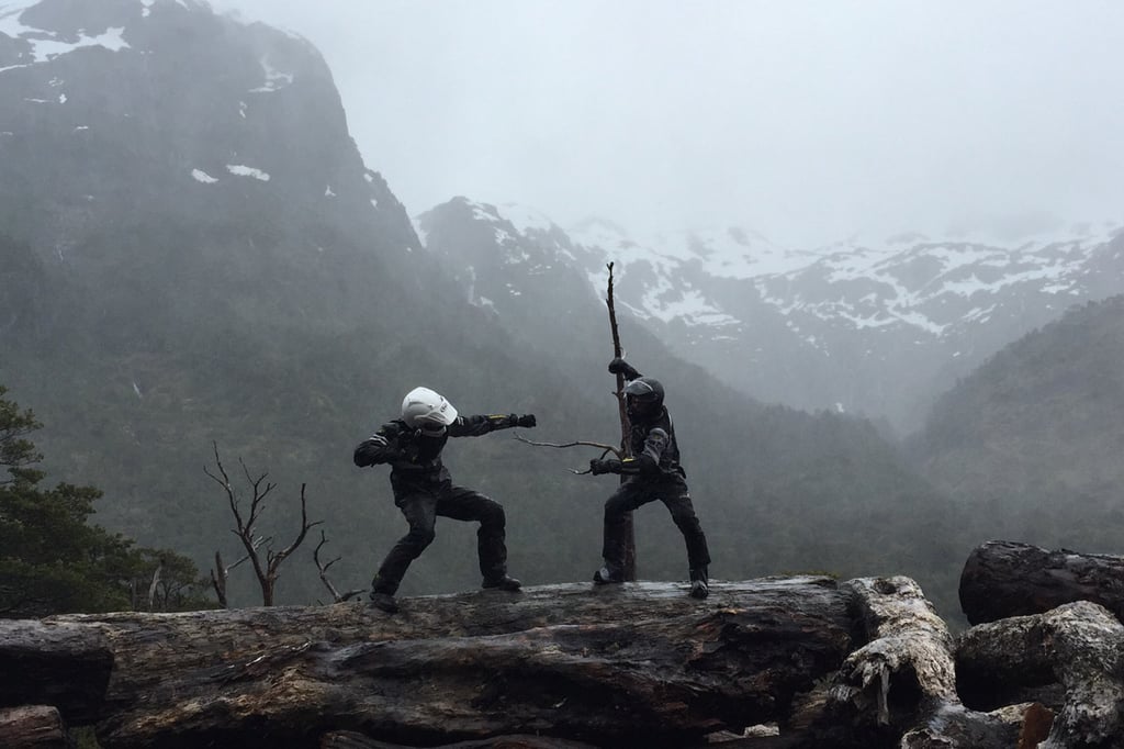 Two Adventure Motorcyclist battling on a log in Patagonia