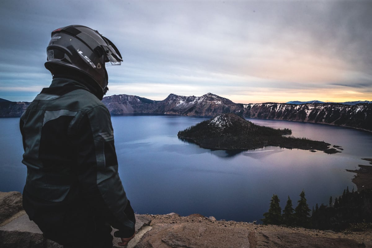 Adventure motorcycle rider looking at Crater Lake from the cliffs edge