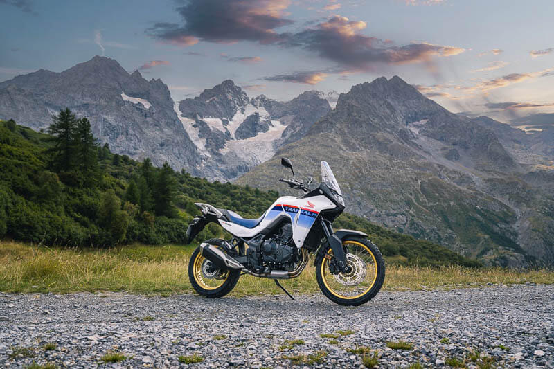 Lonley Honda Transalp motorcycle with huge mountains in the background during sunset.