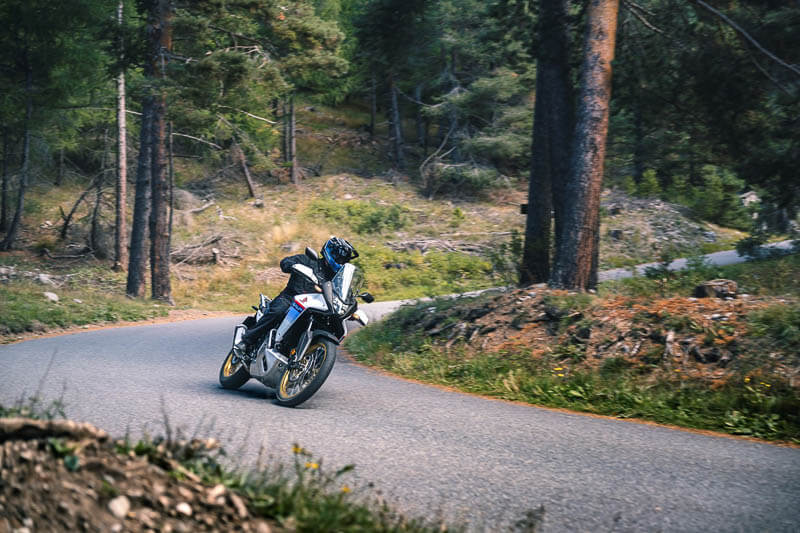 Adventure motorcycle rider taking the Honda Transalp on a tight turn through the forest.