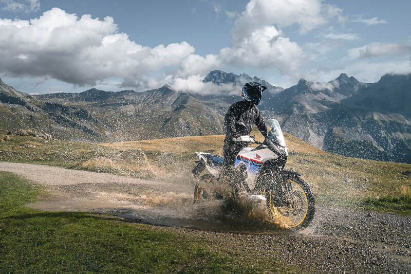 Honda Transalp flying offroad splashing into a large puddle.