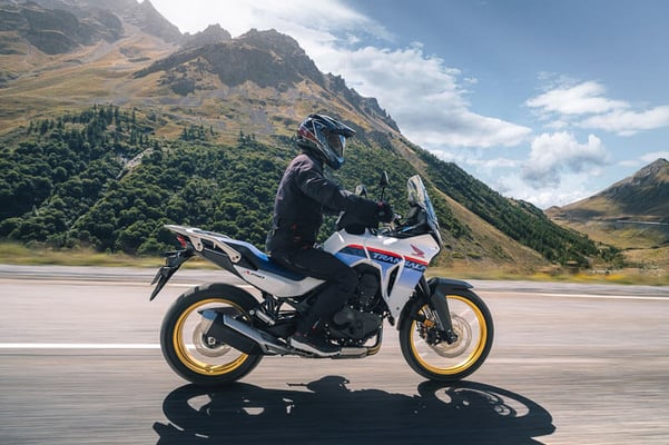 Honda Transalp on a stright away with big green mountains in the background.