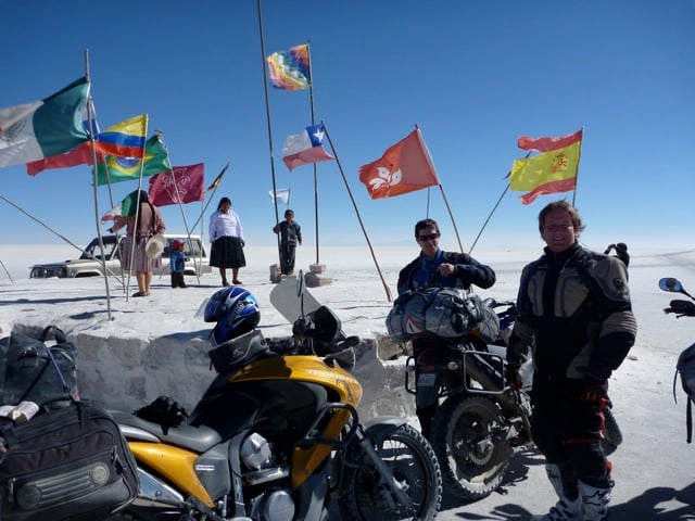 A couple motorcyclists hanging out by prayer flags in Bolivia in the white desert plains..
