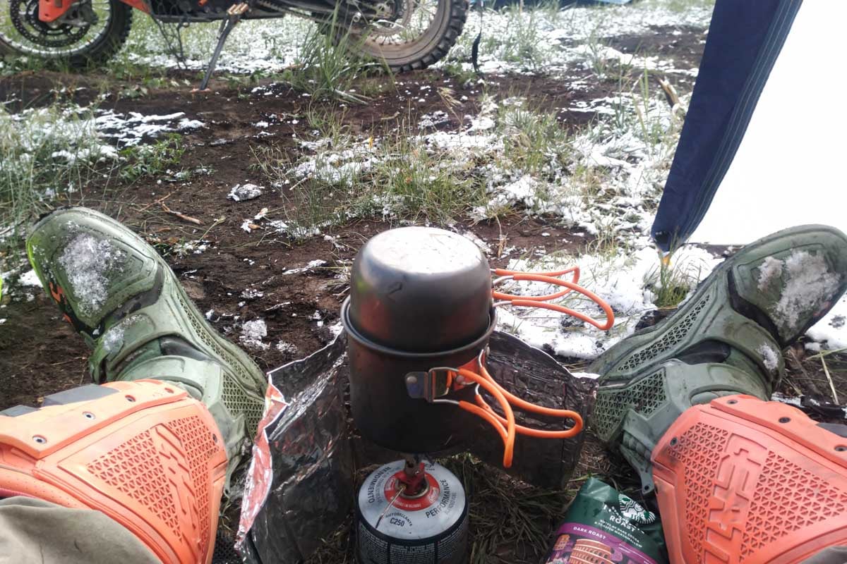 motorcycle rider snow covered boots and camp stove in tent trying to keep warm by heating up coffee on the bdr