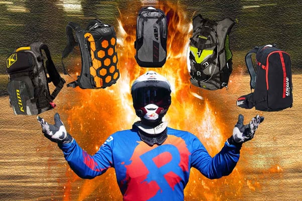 Eric holding up 5 rugged adv motorcycle backpacks with flames in the background.