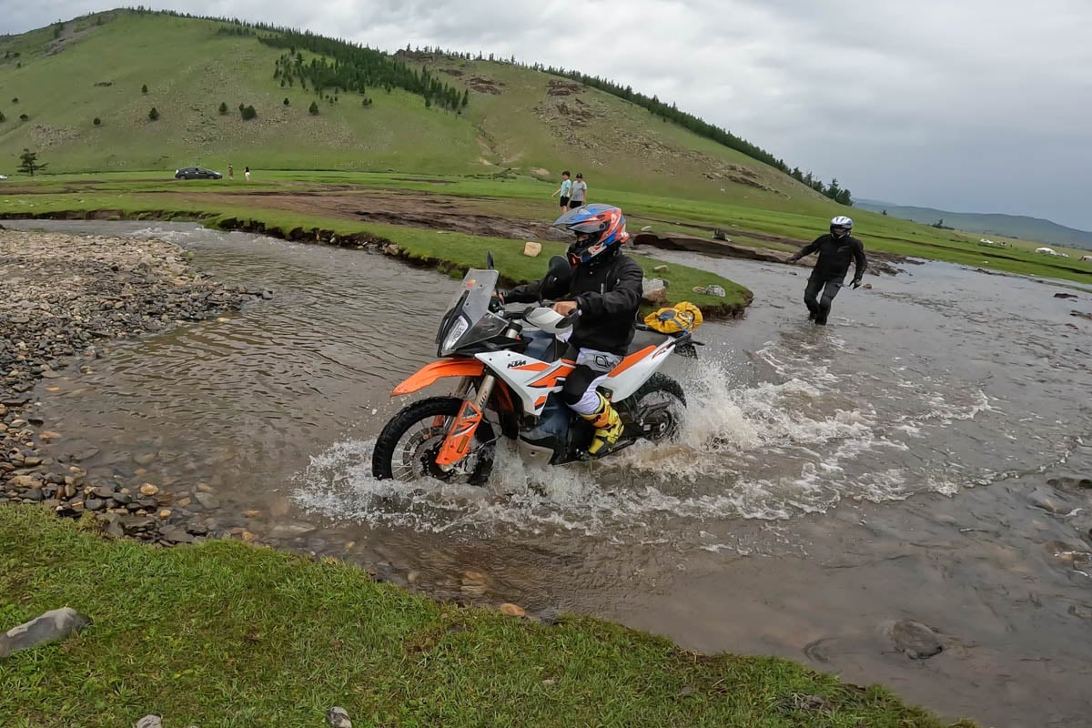 rider goes through difficult section a curved watercrossing while igor walks through behind mongolia