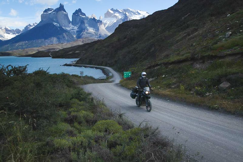 Motorcyclist on a dirt trail with snowy topped mountains in Patagonia.