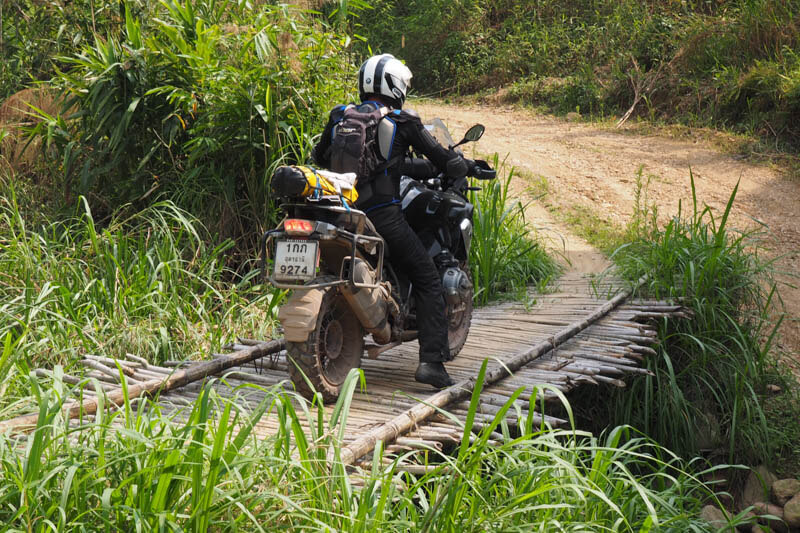 Rider wearing a backpack while riding in Thailand over a bamboo bridge.