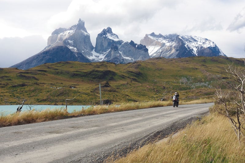 Christine riding through Patagonia on dual sport tires with the famous Torres Del Paine mountains in the background.