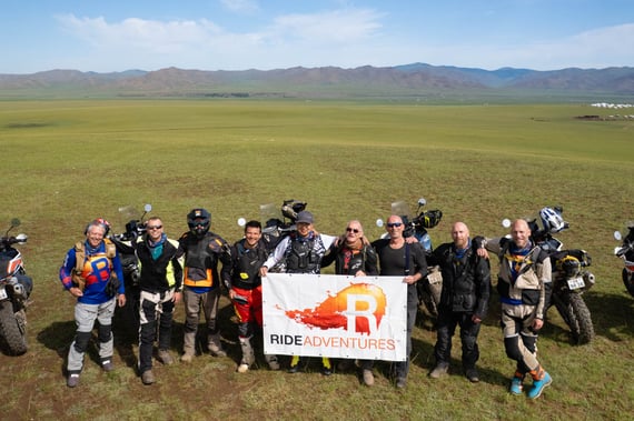 team poses with smiles and laughter in front of RIDE logo banner in Mongolia